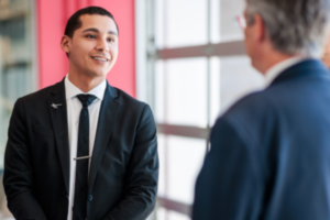 student dressed in a suit and tie talking to another person and smiling.